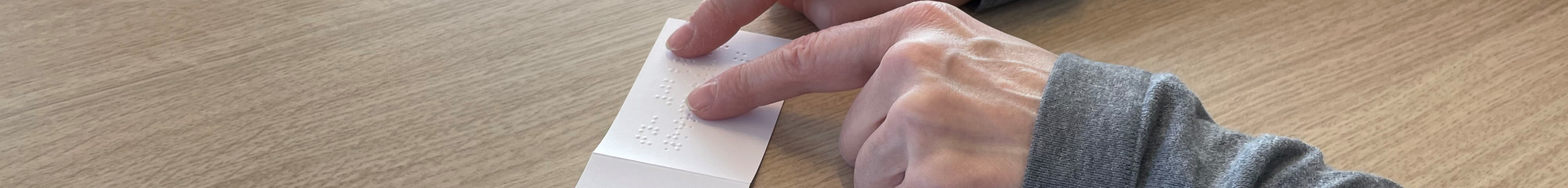 Braille-Schrift auf Zettel wird von einer Hand gelesen